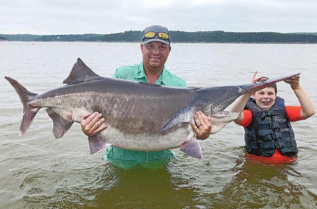 Cody James Watters of Ochelata, with help from son Stetson, 9, holds his rod-and-reel world-record paddlefish that he snagged July 23 at Keystone Lake. (Photo by Eric Brennan/ODWC)